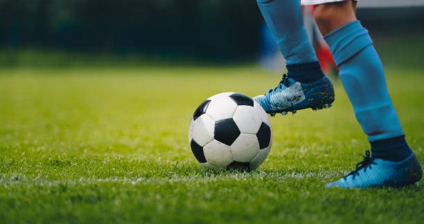 Close up of legs and feet of football player in blue socks and shoes running and dribbling with the ball. Soccer player running after the ball. Sports venue in the background